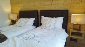 A double bed with white bedding and decorative pillows, flanked by two bedside tables with lamps, in a room with wooden paneling on the walls.