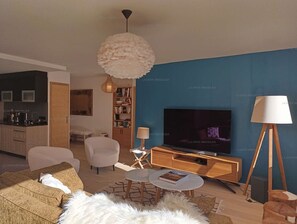 A modern living room with a large flat-screen TV, a round coffee table, and a bookshelf.