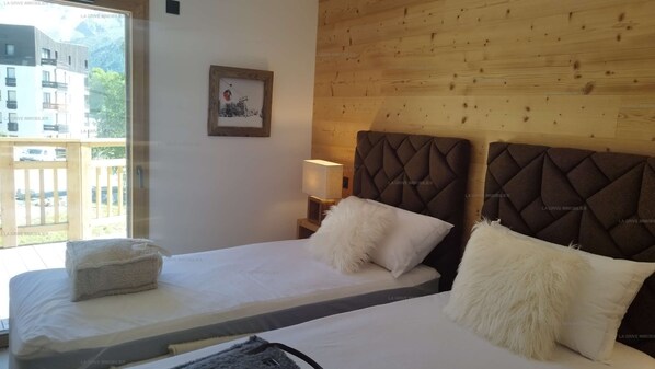 A bedroom with two beds, a wooden headboard, a bedside lamp, and a window with a view of buildings. - Paradiski new, quiet and sunny Plan peisey (PEISEY-NANCROIX)