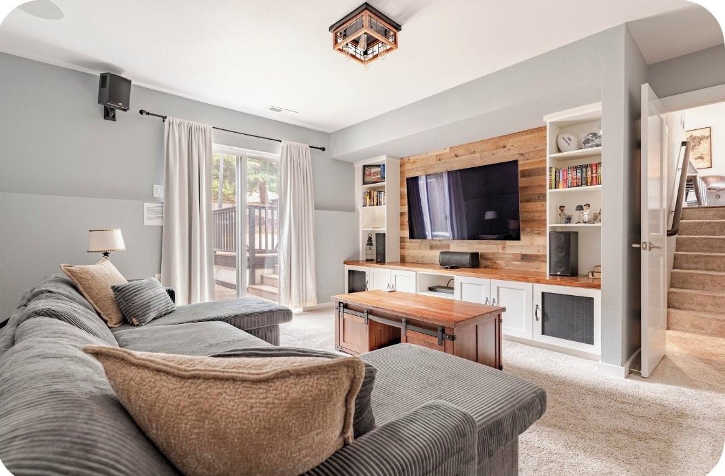 A modern living room with a sectional sofa, a flat-screen TV, a wooden accent wall, and a bookshelf.