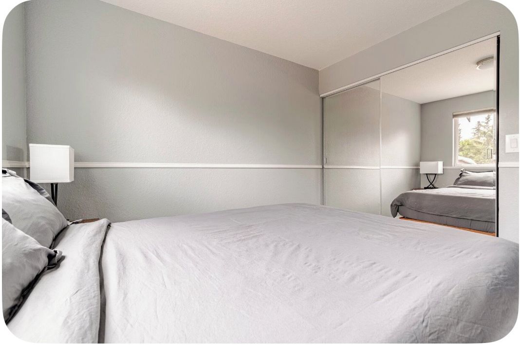 A bedroom with a bed, a bedside table, a lamp, and a large mirror.