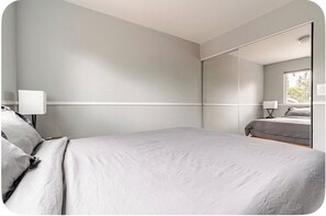 A bedroom with a bed, a bedside table, a lamp, and a large mirror.