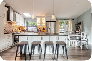 A modern kitchen with a central island, bar stools, and a dining area with white chairs.