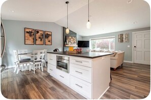 A modern kitchen with white cabinetry, a central island, and a dining area with white chairs.