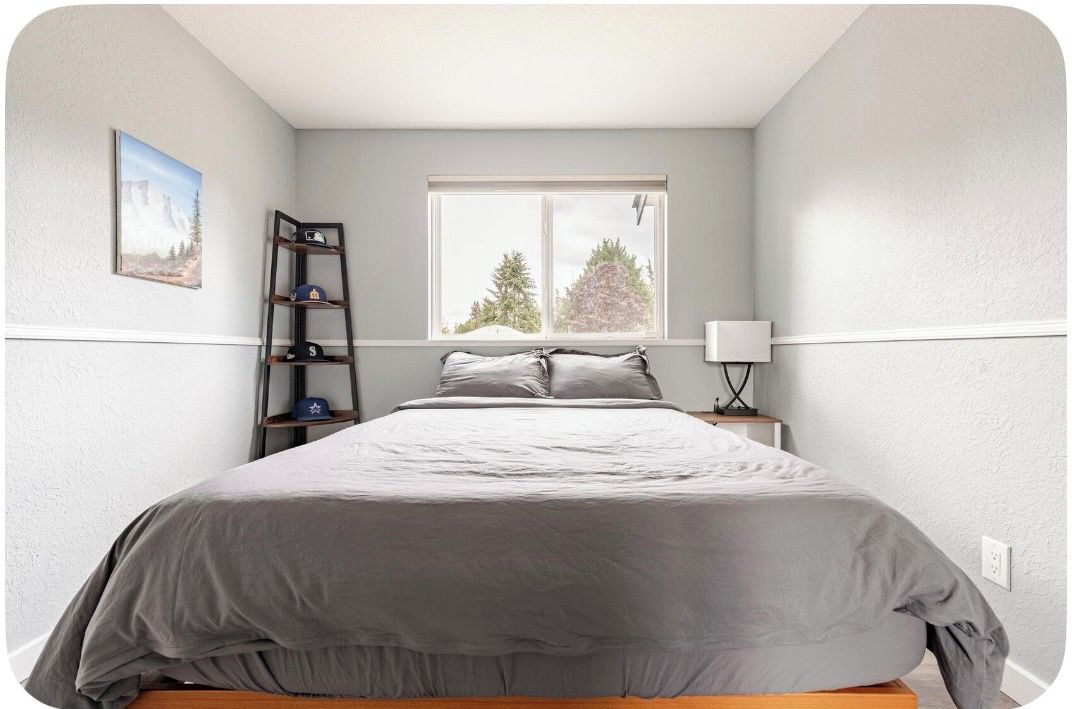 A bedroom with a bed, a window, a nightstand, a lamp, and a shelf with hats.