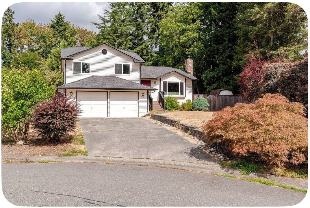 A two-story residential house with a garage, surrounded by trees and shrubs.