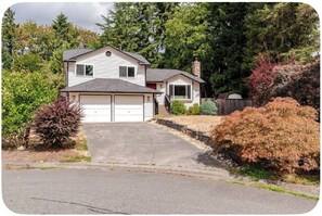 A two-story residential house with a garage, surrounded by trees and shrubs.