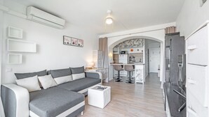 A modern living room with a grey sectional sofa, a white coffee table, and a kitchen area visible through an archway. - WELCS ESTUDIO 213 EMP con piscina comunitaria (Rosas / Roses)