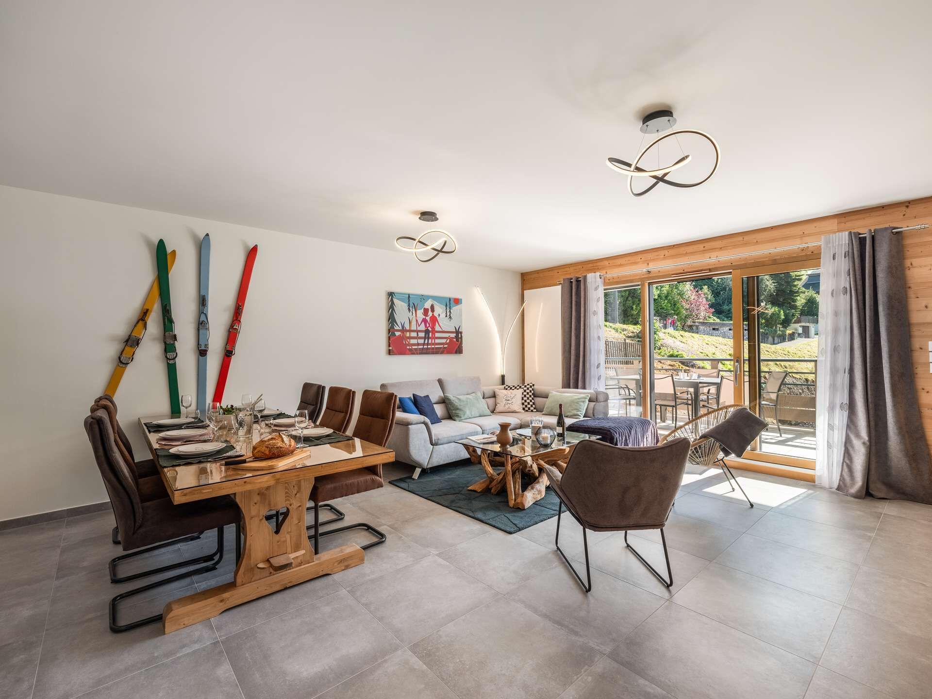 Un vaste espace de vie comprenant une table à manger, un canapé et des fauteuils, un tableau accroché au mur et une vue à travers la porte vitrée.