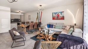 En moderne stue med spiseplads, en sofa, et sofabord og et billede på væggen.