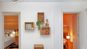 Et værelse med en seng, et natbord, en lampe, et indrammet billede, en træhylde med en plante og en lille trækasse.