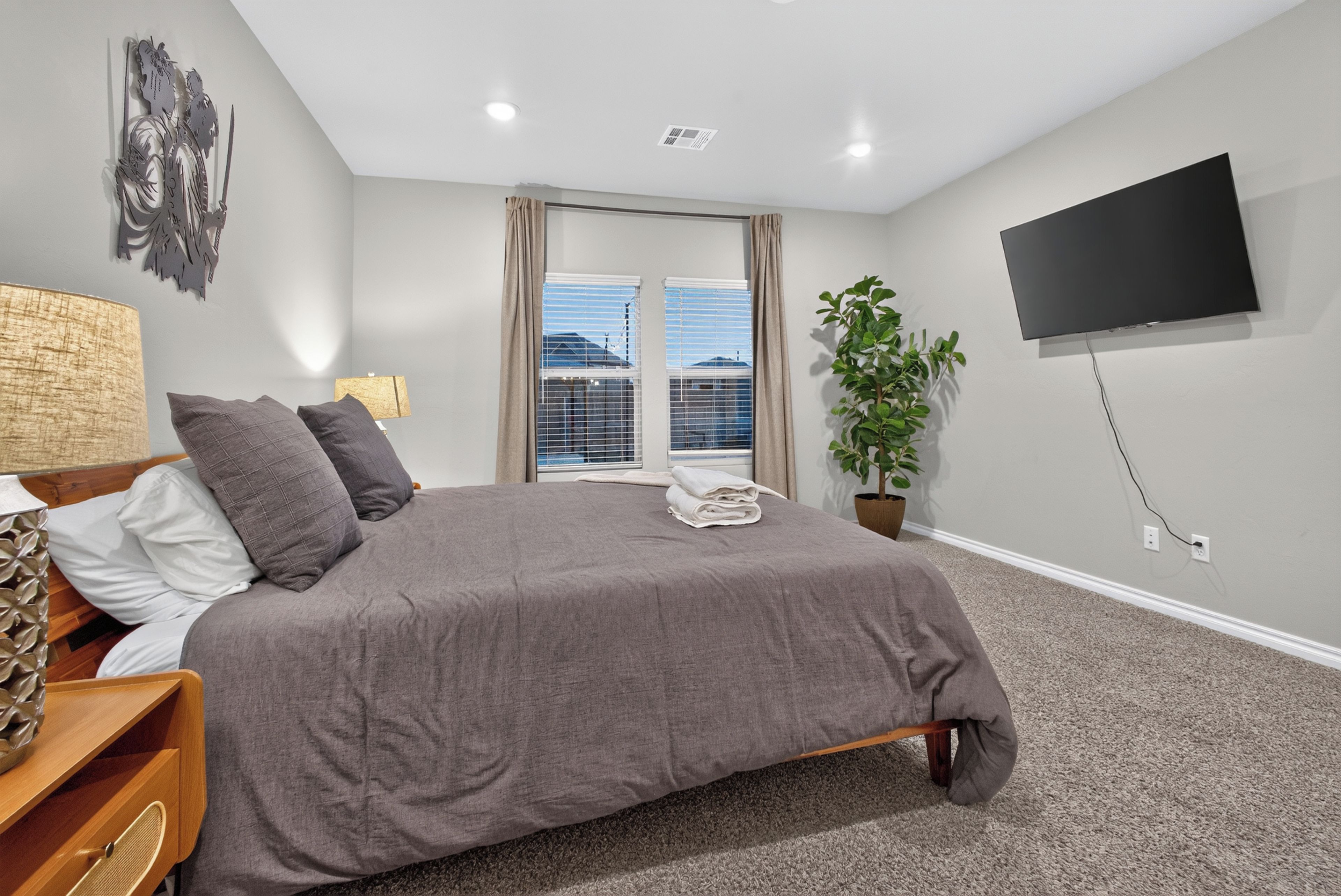 Quarto com cama, televisão, planta e janela com persianas.