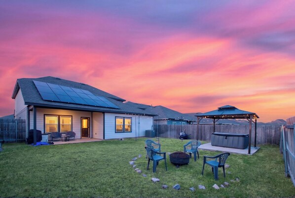 A residential backyard with a covered patio area, outdoor seating, and a hot tub.