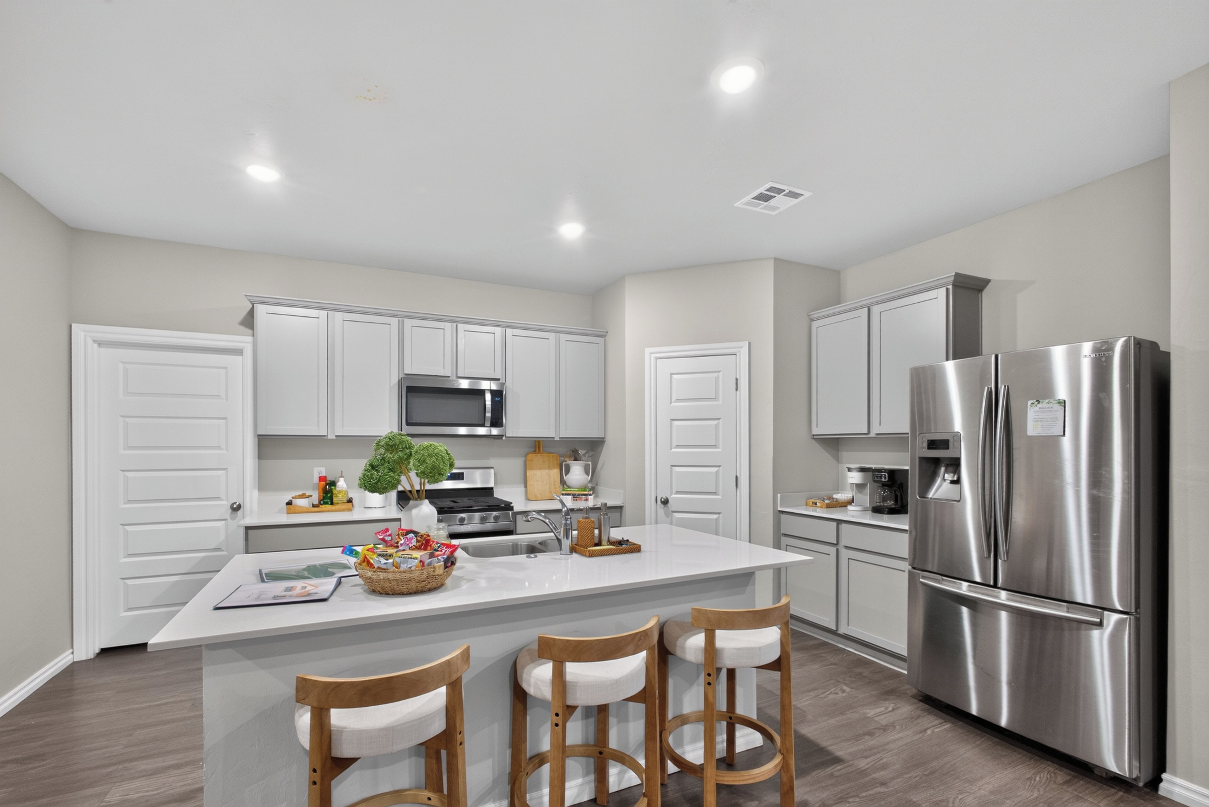 A modern kitchen with white cabinetry, stainless steel appliances, and a central island with bar stools.