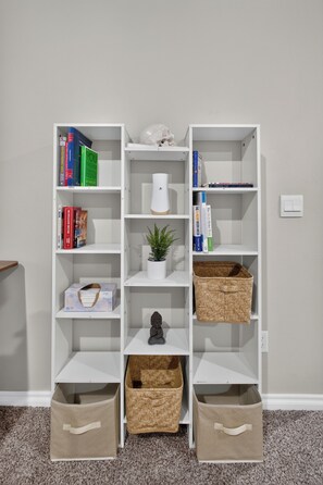 A white shelving unit with books, a potted plant, a small statue, and two storage baskets.