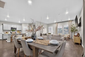 Una cucina moderna con mobili bianchi, una zona pranzo con tavolo in legno e un soggiorno con divano e TV a parete.