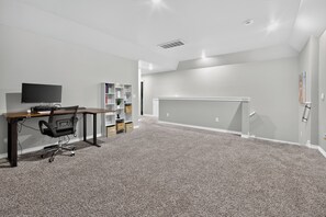 A room with a desk, chair, bookshelf, and a flat-screen TV.