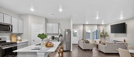 A modern kitchen with a central island, stainless steel appliances, and a dining area with a flat-screen TV.