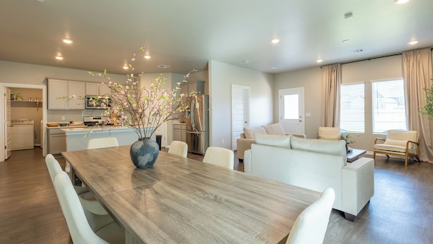 A modern kitchen with white cabinets, a dining area with a wooden table, and a living room with a sofa and chairs. - KING SIZE  6BED HOME + 6 PERSON HOT TUB + FIREPIT (Yukon)