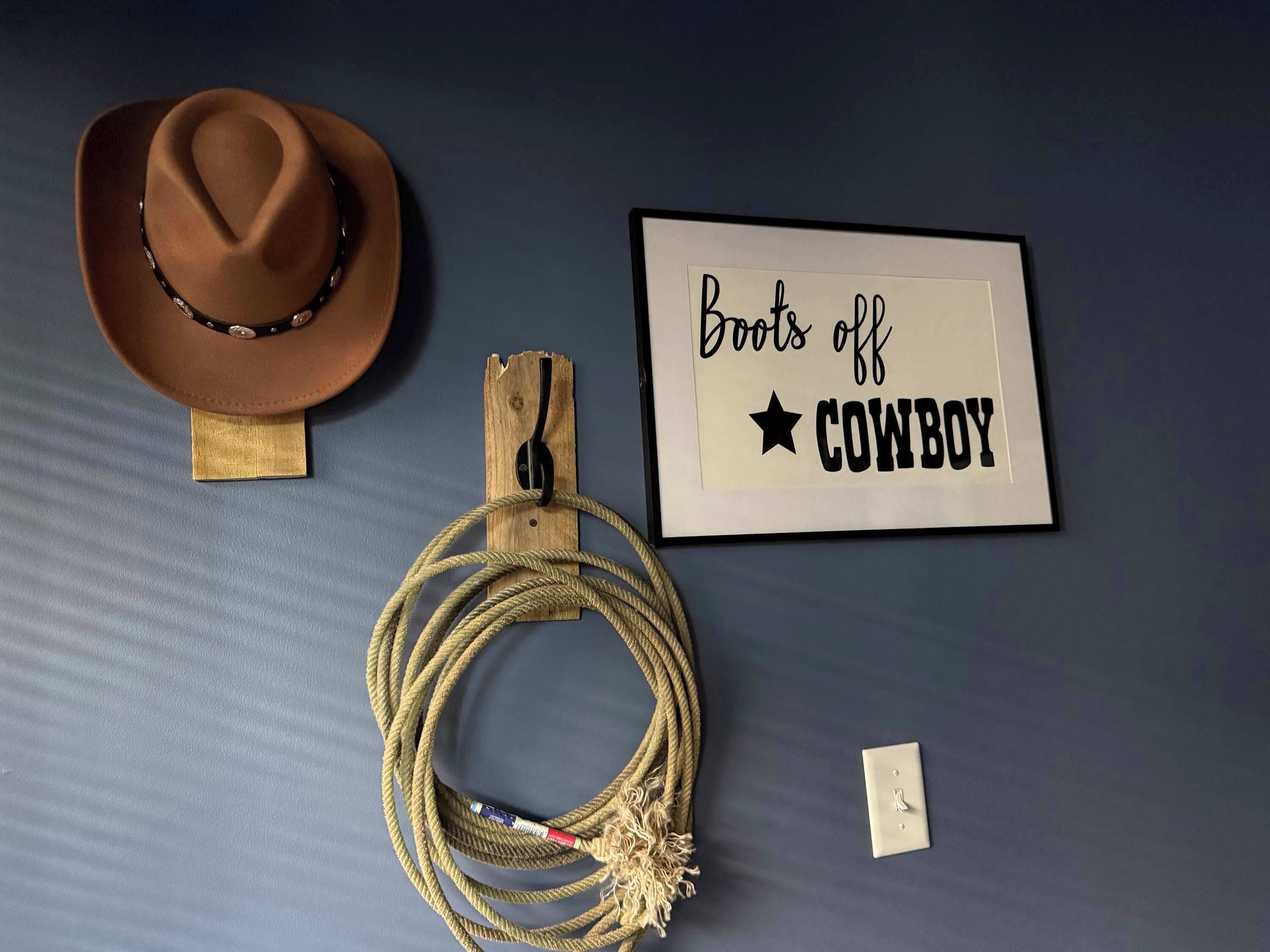Um chapéu de cowboy, uma corda e uma placa emoldurada com o texto 'Boots off COWBOY'.