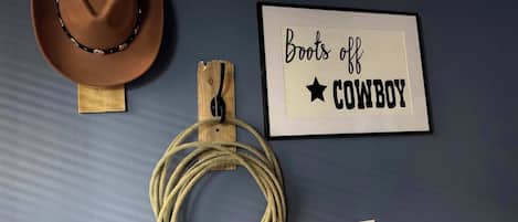 Um chapéu de cowboy, uma corda e uma placa emoldurada com o texto 'Boots off COWBOY'.