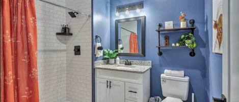 A bathroom with a shower, white cabinets, a sink, a toilet, and a mirror.