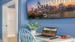 Une pièce avec un ordinateur portable sur un bureau, une chaise, une plante en pot et une assiette de fraises. Une grande enseigne indique : « Bienvenue à Nashville » et « Chady, gestion immobilière ».