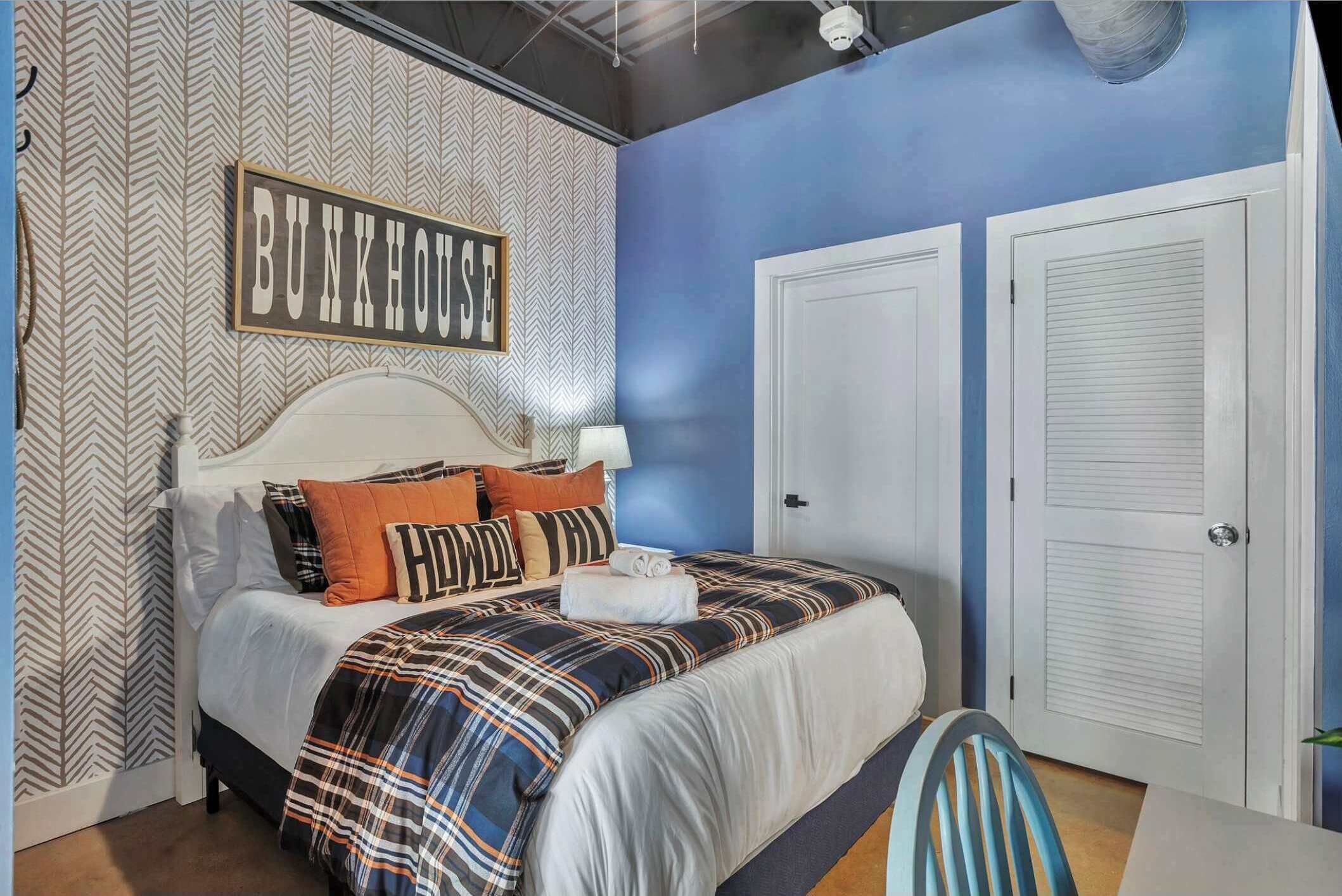 Un dormitorio con una cama, cabecera, un cartel en la pared que dice "BUNKHOUSE" y dos puertas cerradas.