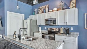 Une cuisine moderne avec des meubles blancs, des plans de travail en granit, des appareils électroménagers en acier inoxydable et un mur d’accent bleu.