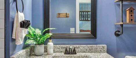 A bathroom with a blue wall, a granite countertop, a white sink, and a mirror with three lights.