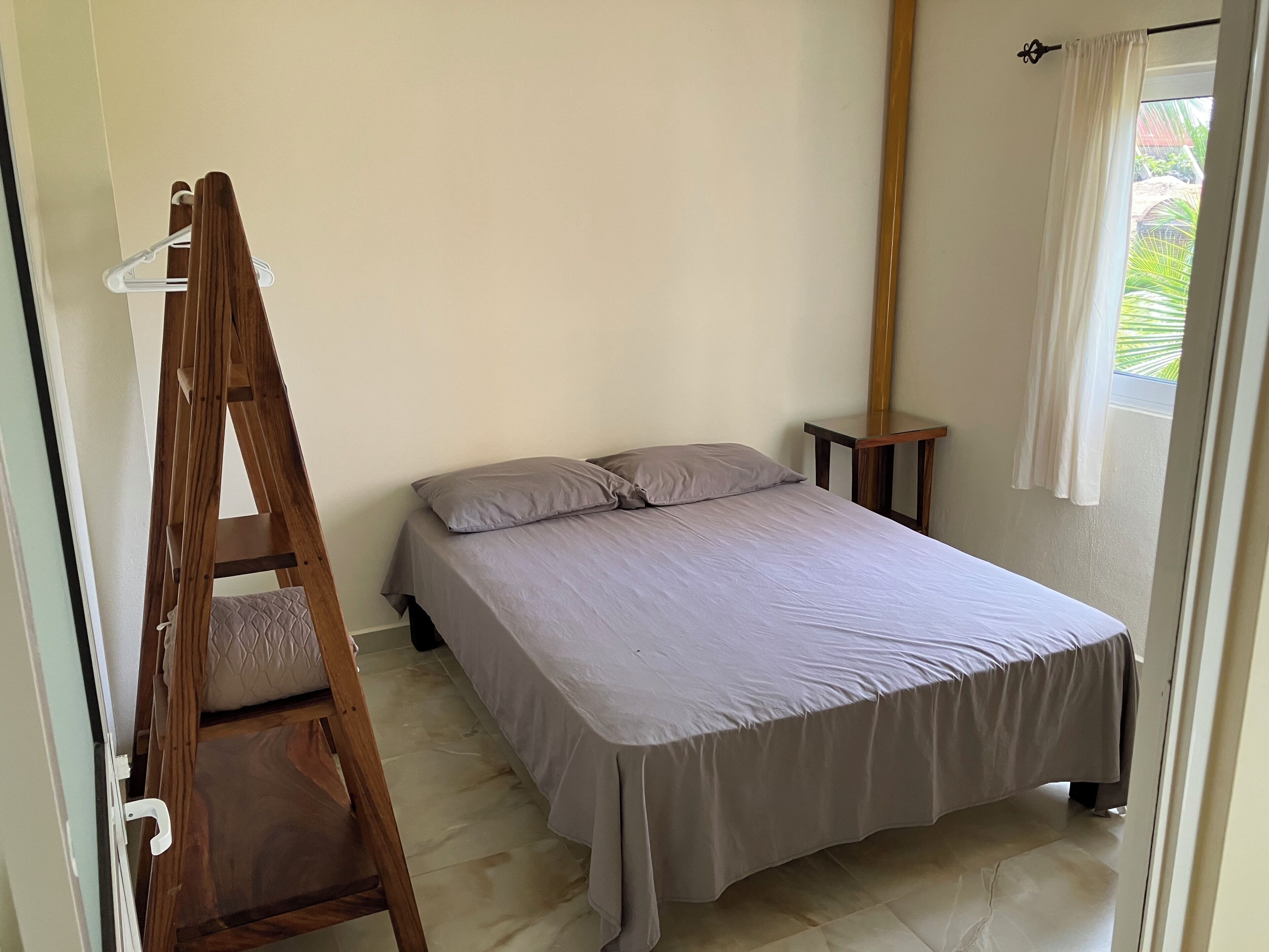 A bedroom with a bed, a wooden ladder, a nightstand, and a window with curtains.