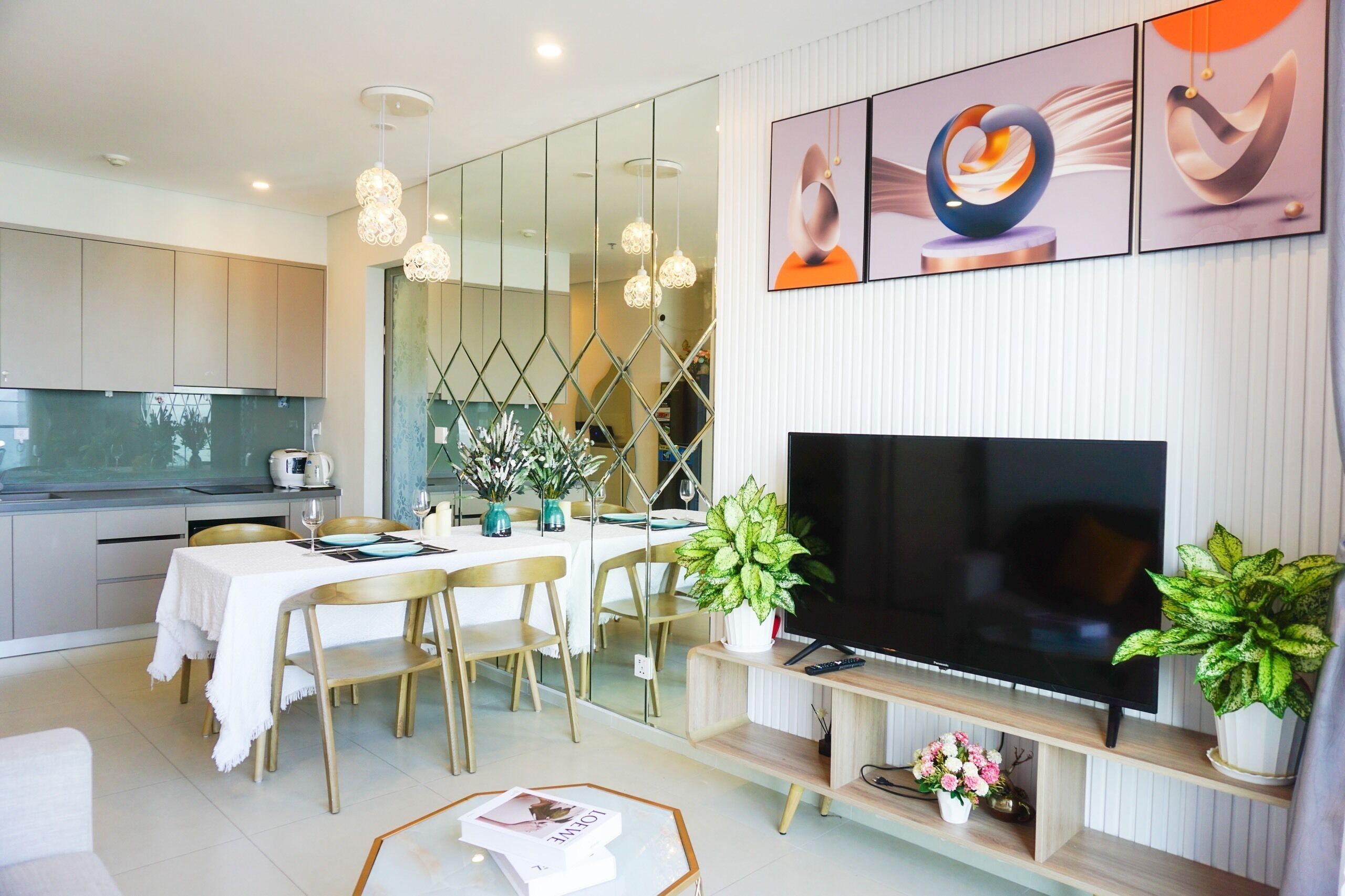 Una sala moderna con televisor de pantalla plana, comedor con sillas y una mesa, y una cocina al fondo.