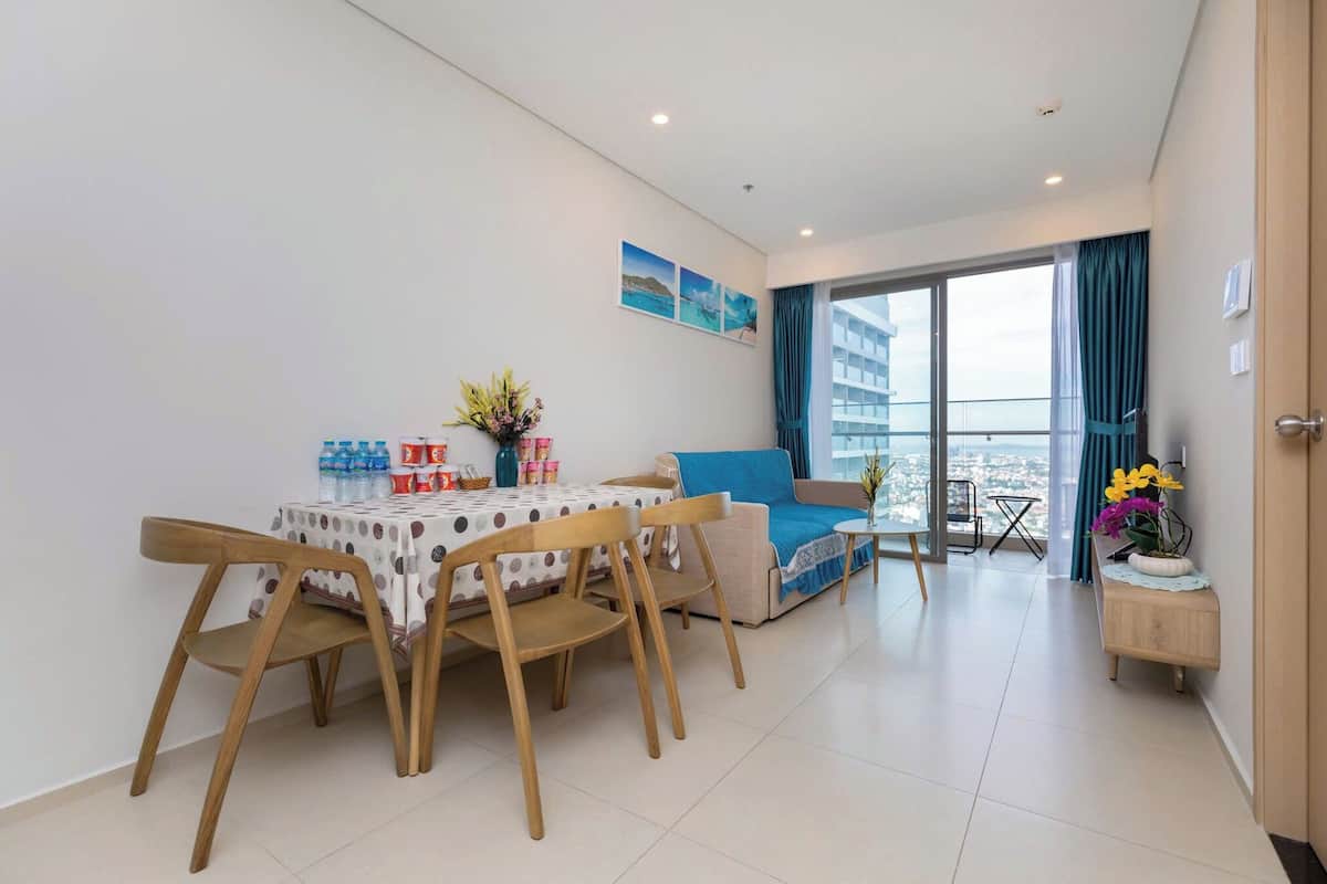 A modern living room with a dining area, a sofa, and a balcony with a city view.