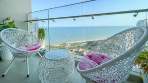 Ein Balkon mit zwei weißen Korbstühlen und einem kleinen runden Tisch, mit Blick auf die Küste.