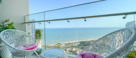 Een balkon met twee witte wicker stoelen en een klein rond tafeltje, met uitzicht op de kust.