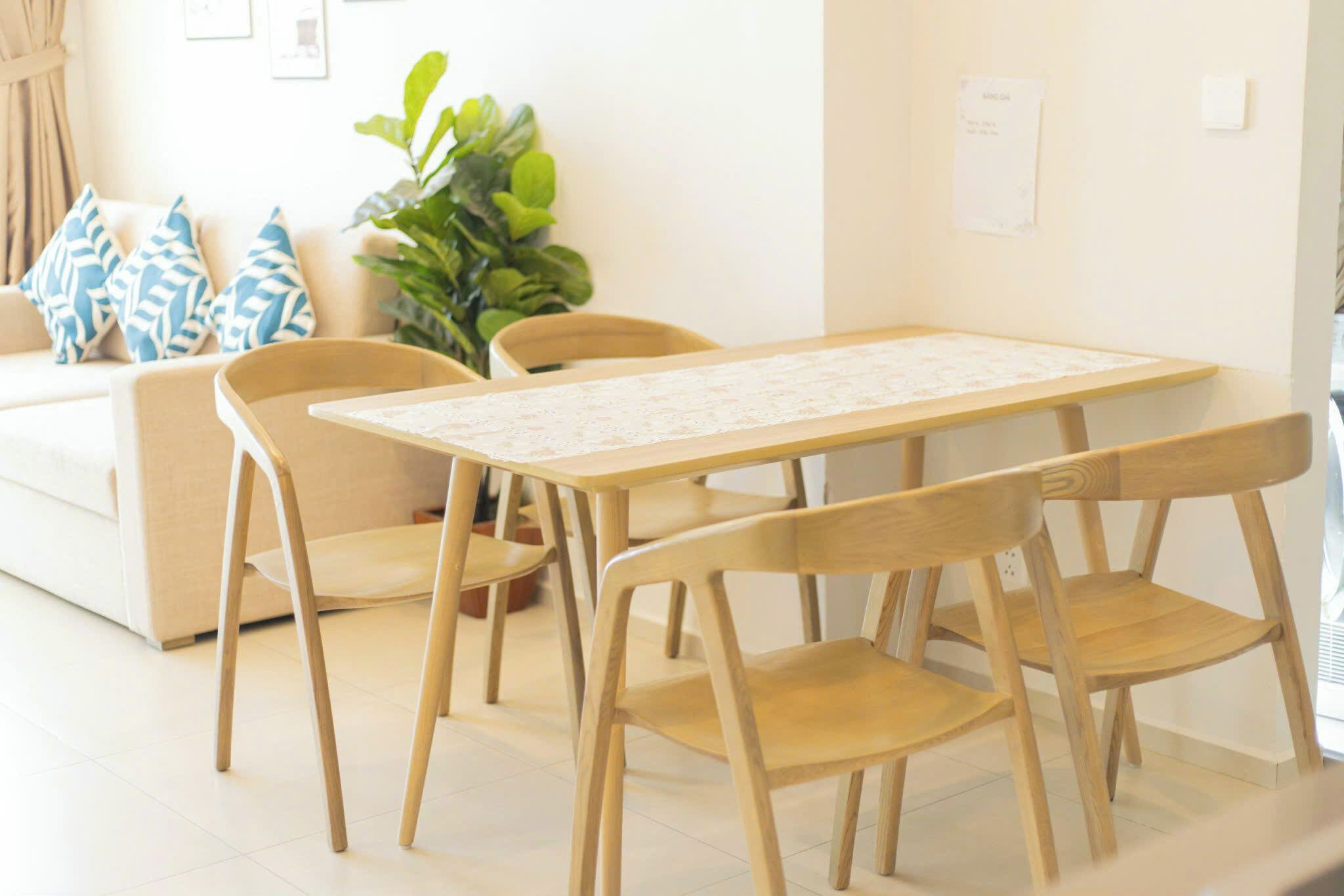 Zona pranzo con tavolo e sedie in legno, un divano con cuscini decorati e una pianta verde.
