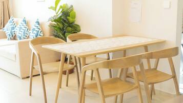 Zona pranzo con tavolo e sedie in legno, un divano con cuscini decorati e una pianta verde.