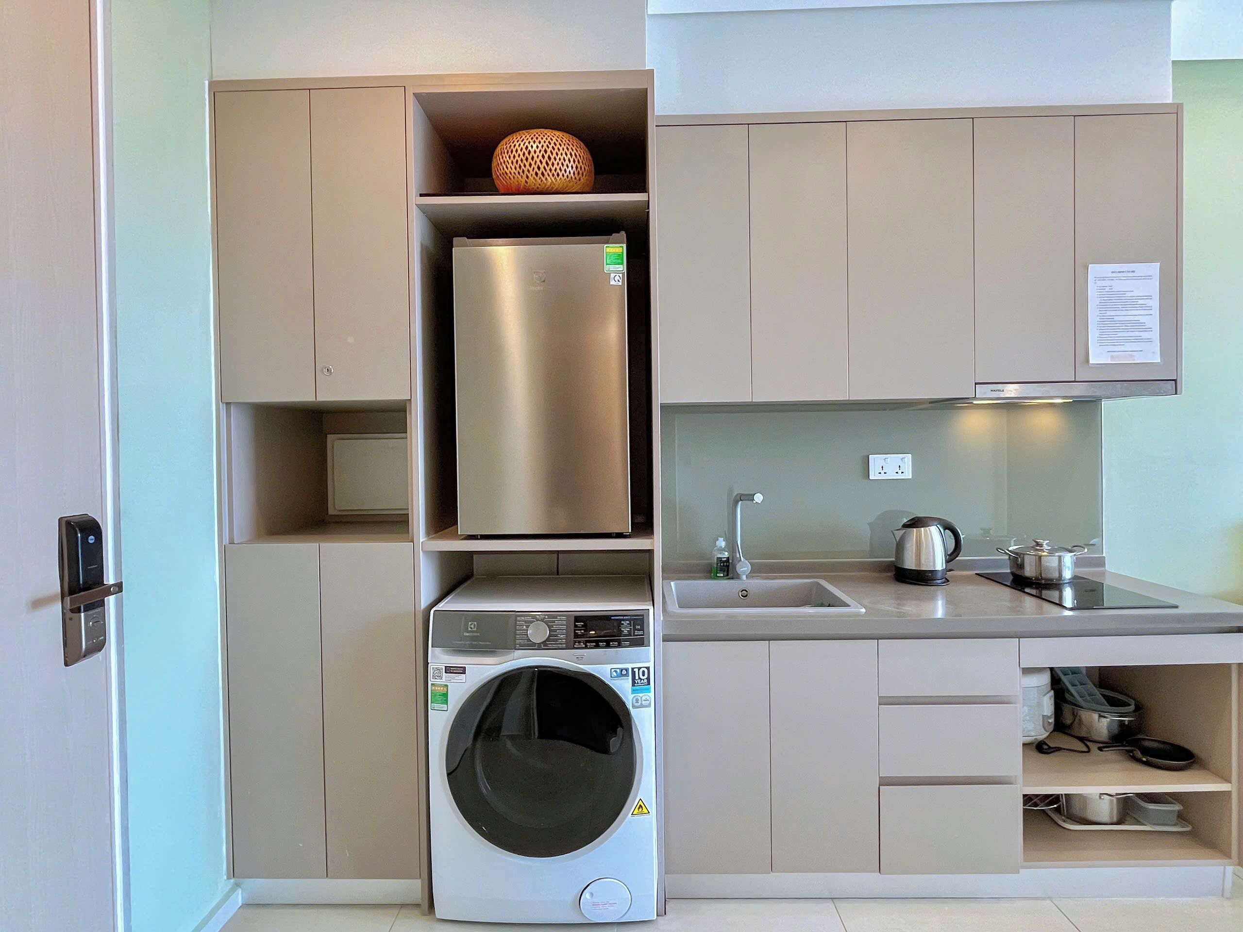 A compact kitchen with a built-in washer and dryer, stainless steel appliances, and a small countertop with a kettle and pots.