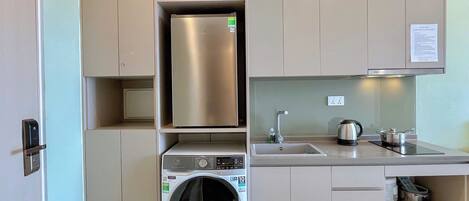 A compact kitchen with a built-in washer and dryer, stainless steel appliances, and a small countertop with a kettle and pots.