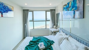 Ein Schlafzimmer mit großem Fenster, einem Bett mit türkisfarbener Decke und Kunstwerken an den Wänden.