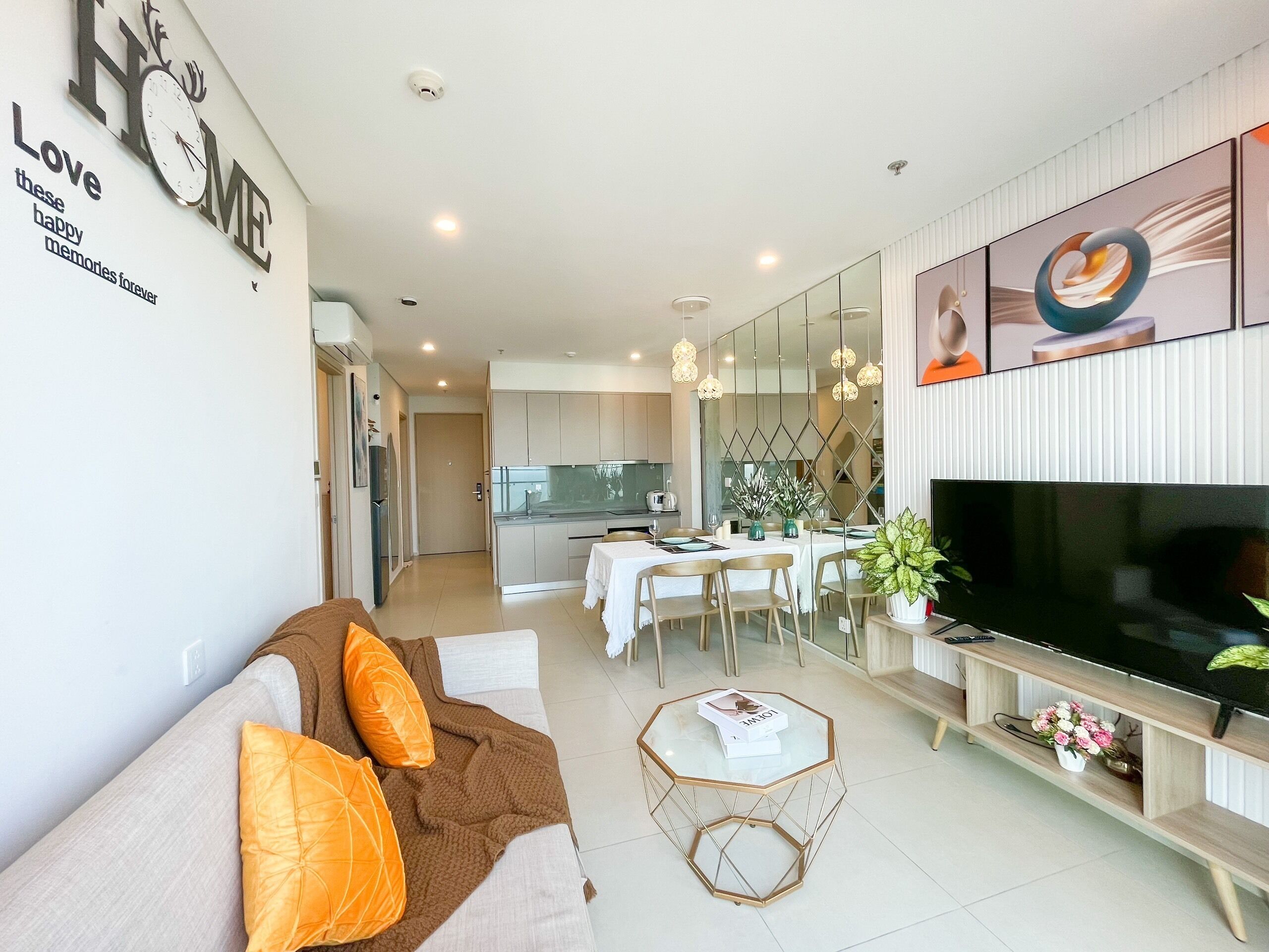 Una sala moderna con sofá, mesa de centro y televisor. Se observa un comedor con mesa y sillas al fondo.