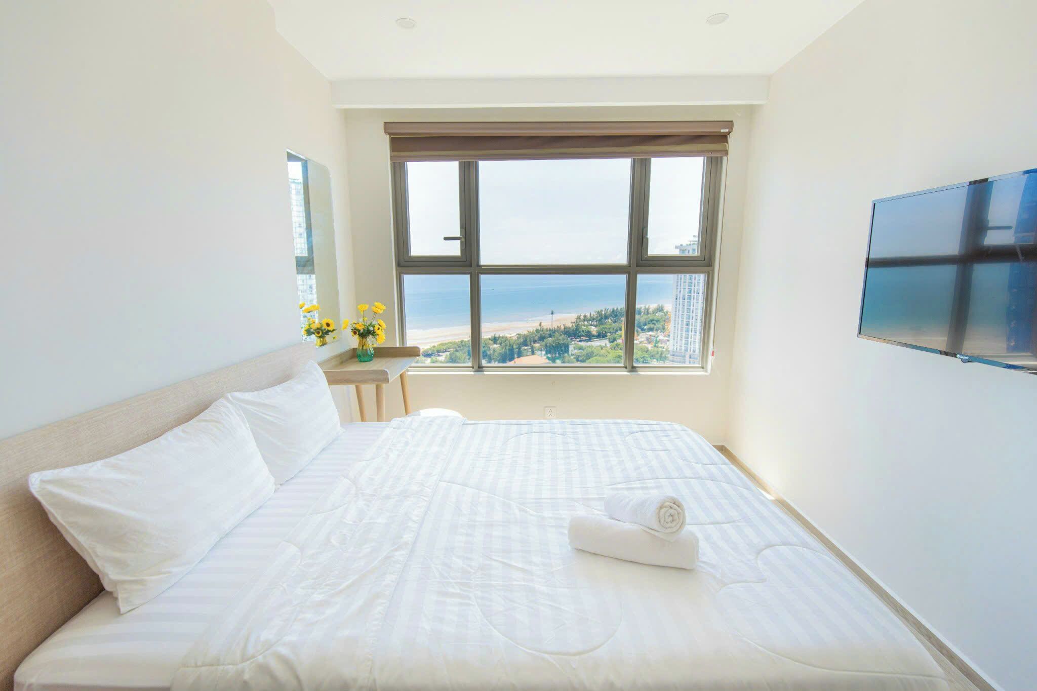 Ein Hotelzimmer mit einem großen Bett, einem an der Wand montierten Fernseher und einem Fenster mit Blick auf den Strand.