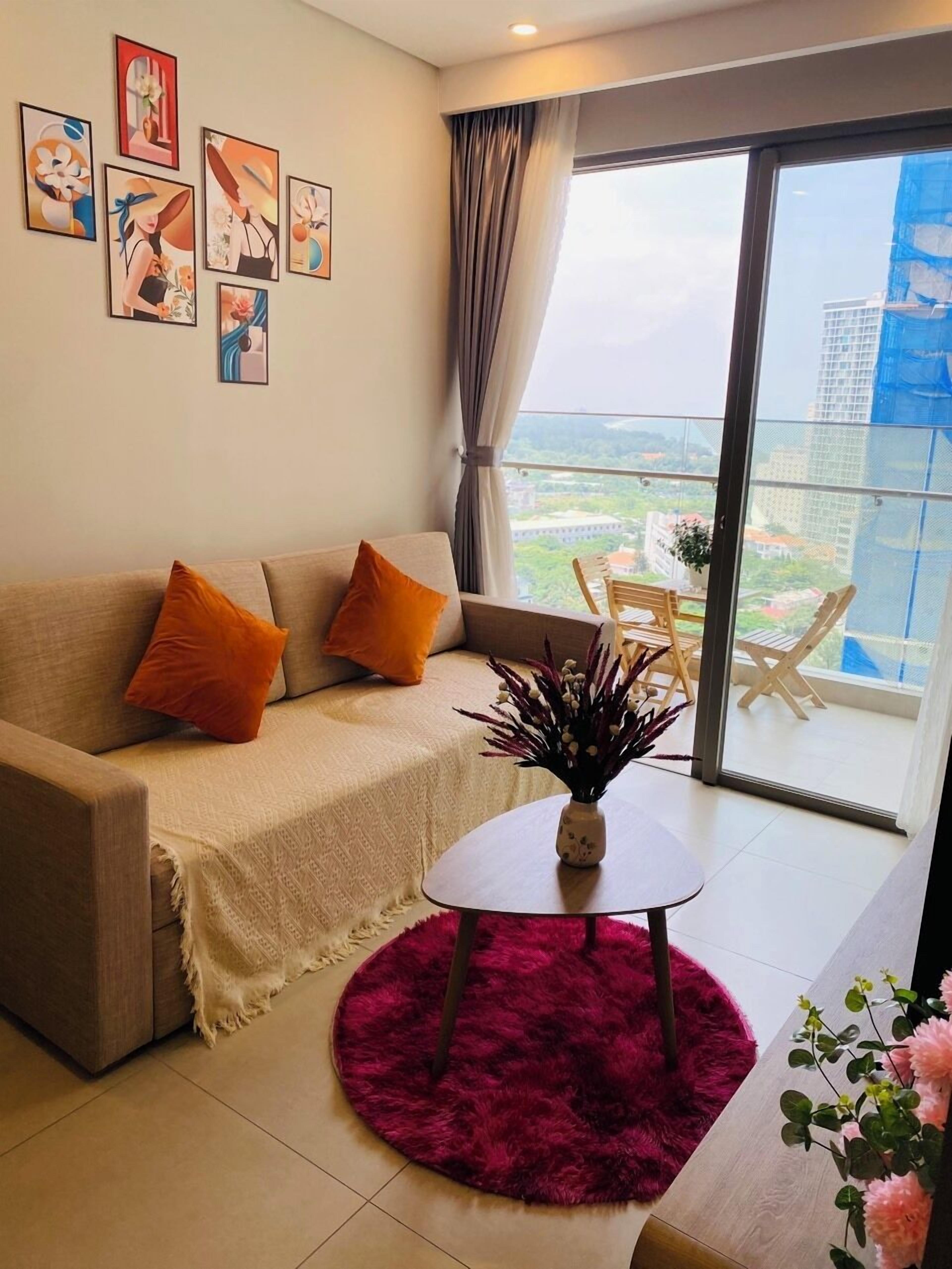 A modern living room with a sofa, a small round table, and a view of a balcony with outdoor furniture.