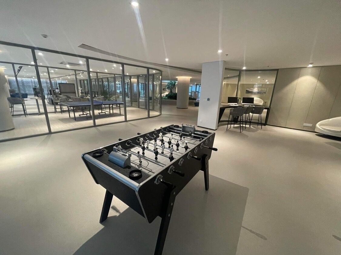 A modern indoor space with a foosball table, glass partitions, and a seating area with tables and chairs.
