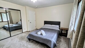 Quarto com cama, mesa de cabeceira, espelho e porta.