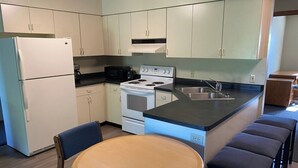 Una cocina compacta equipada con refrigerador, microondas, estufa y pileta. Cuenta con una mesa redonda de madera y cuatro taburetes altos.