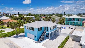Un bâtiment bleu avec un escalier, un espace piscine avec des chaises longues, et un bâtiment blanc au premier plan.