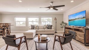 Un salon moderne comprenant un canapé, deux fauteuils, une table basse, un téléviseur et un ventilateur de plafond.