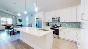 A modern kitchen with white cabinets, a large island, stainless steel appliances, and pendant lighting. - Delightful 3-bedroom house in Bradenton with WiFi, Games, and more #1 of 2 (Bradenton)