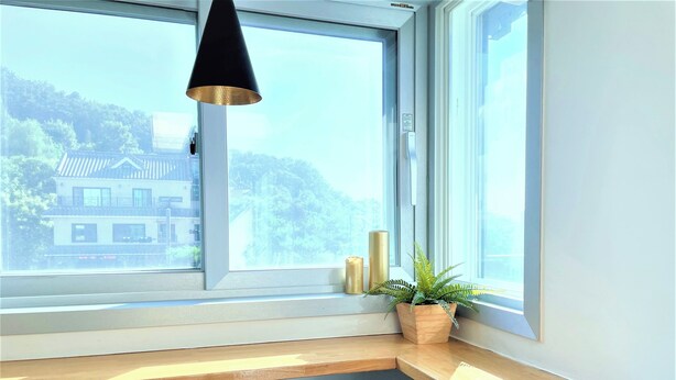 A corner desk with a chair, a potted plant, and a window with a view of buildings and trees. - Incheon airport W Premium guesthouse (Incheon)